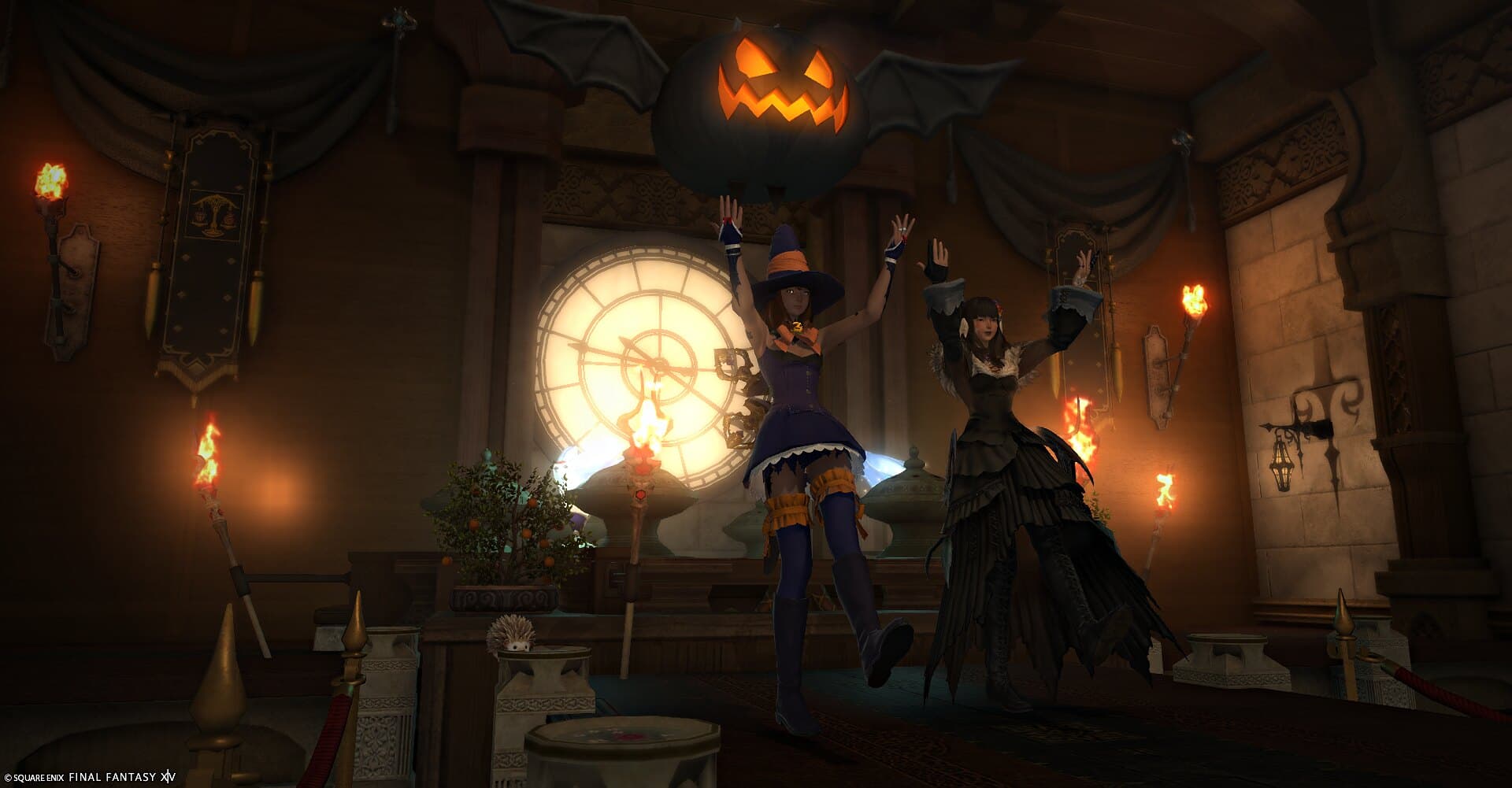 Two guests in costume with arms raised on the runway, beneath a giant floating jack-o'-lantern and between burning torches