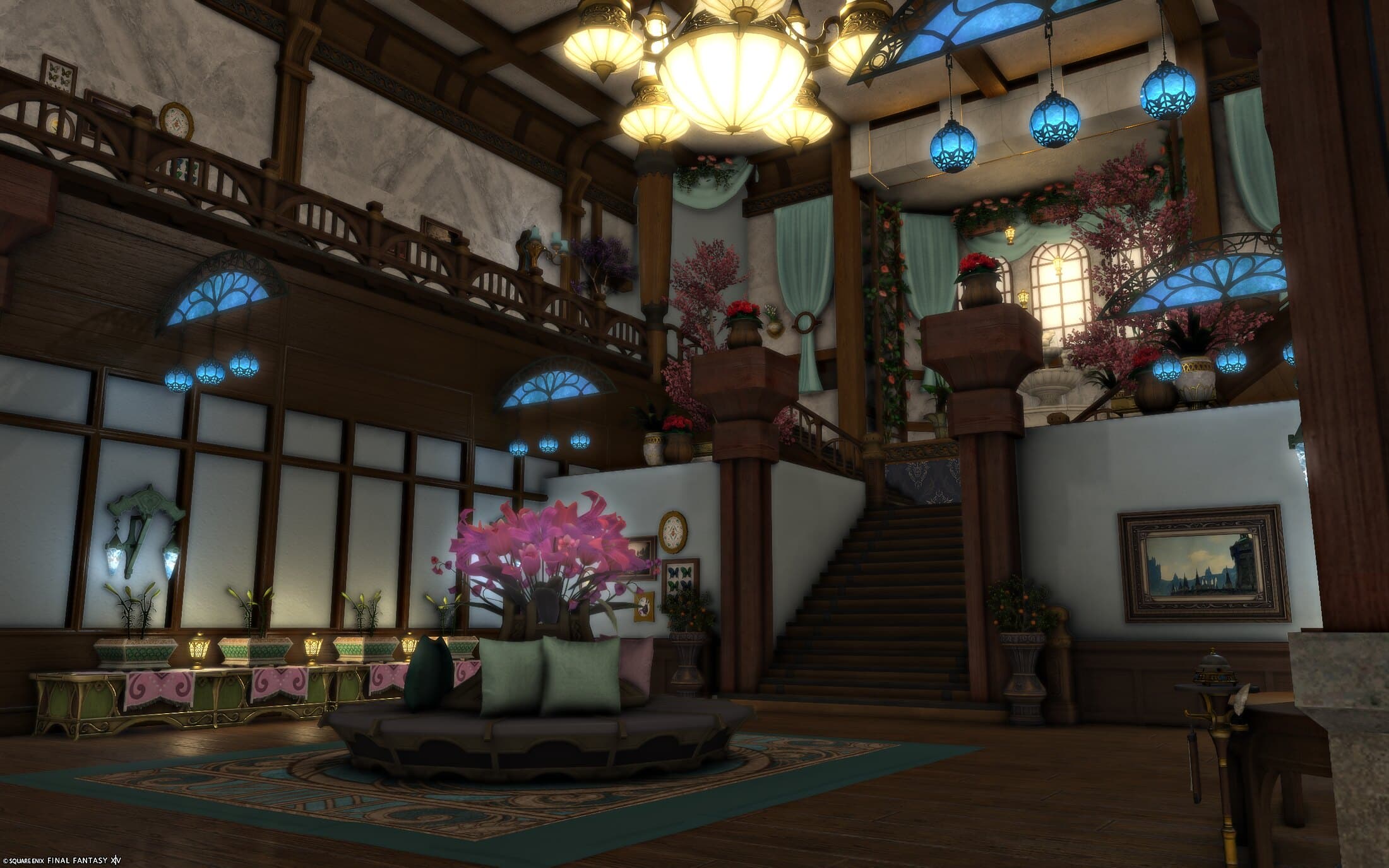 The entry hall — a round seat of pink flowers and pale cushions on a teal rug, a staircase climbing to the fountain landing hung with teal curtains, pink-blossomed trees and red flowers in urns on the stair pillars, lamps of blue glass hung with glowing blue lanterns, and a chandelier overhead