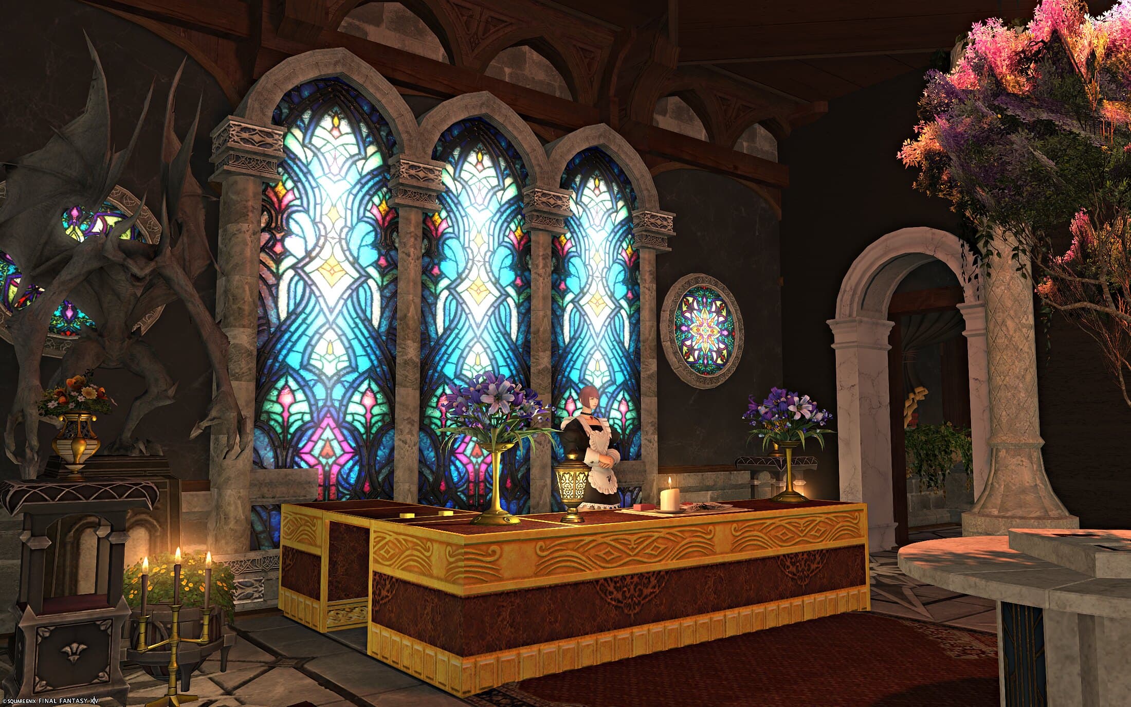 The reception counter in gold and red set against three tall stained-glass windows, an attendant behind it and a stone gargoyle at the left