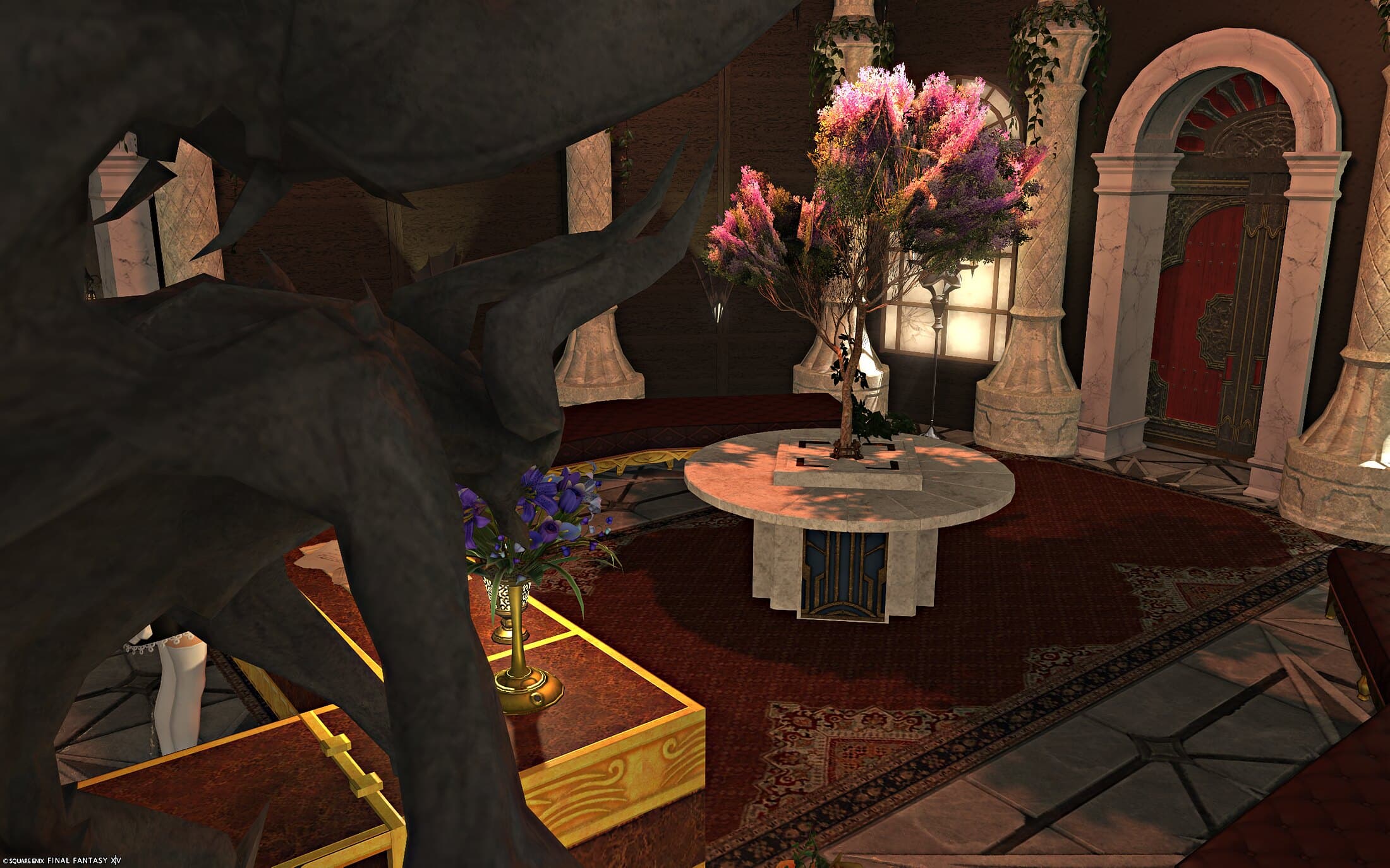 The gargoyle close up in the foreground, the blossoming tree on its marble table and the red front door beyond