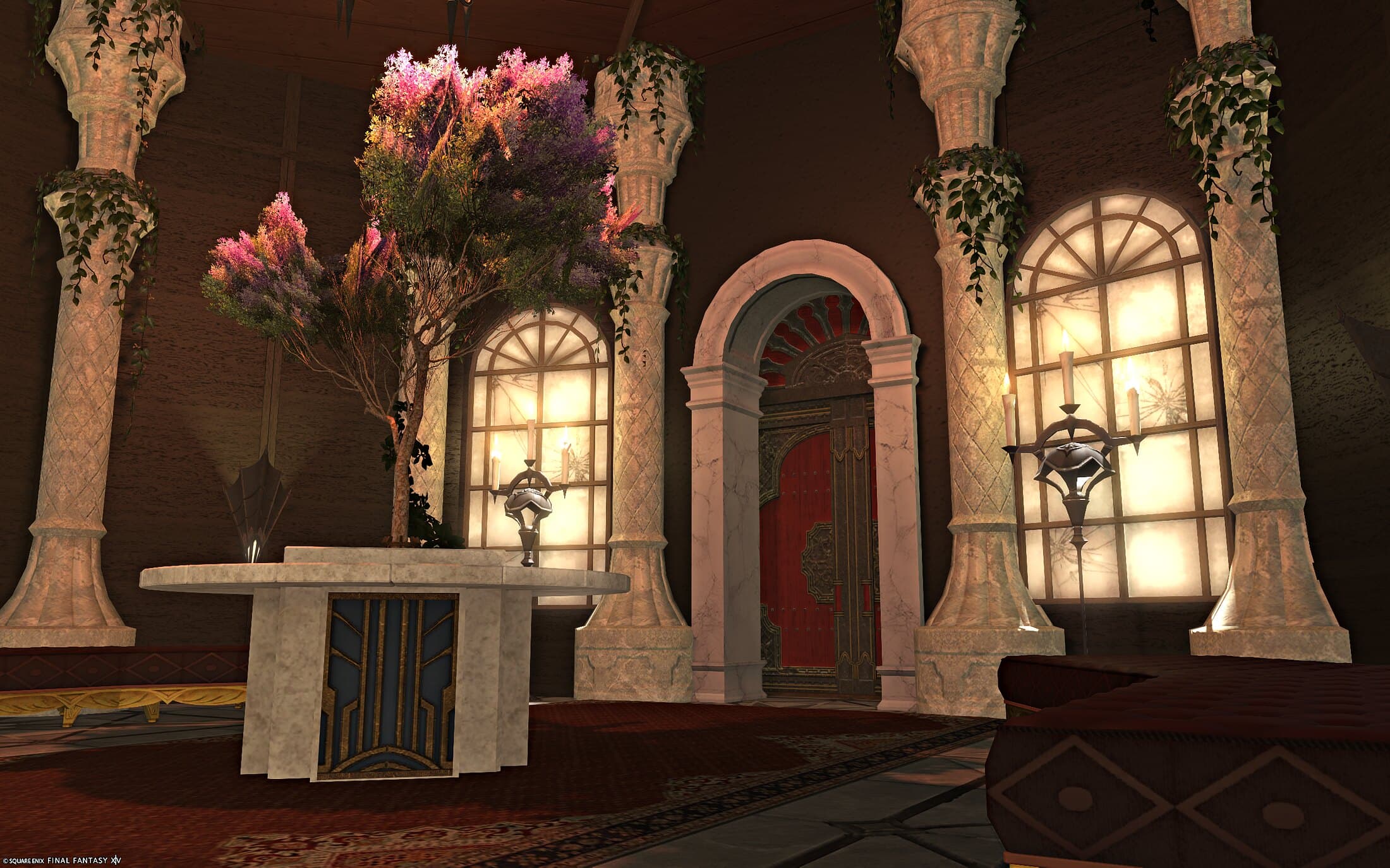 A blossoming tree on a round marble table between ivory pillars, candle sconces on the frosted arched windows and a red door beyond