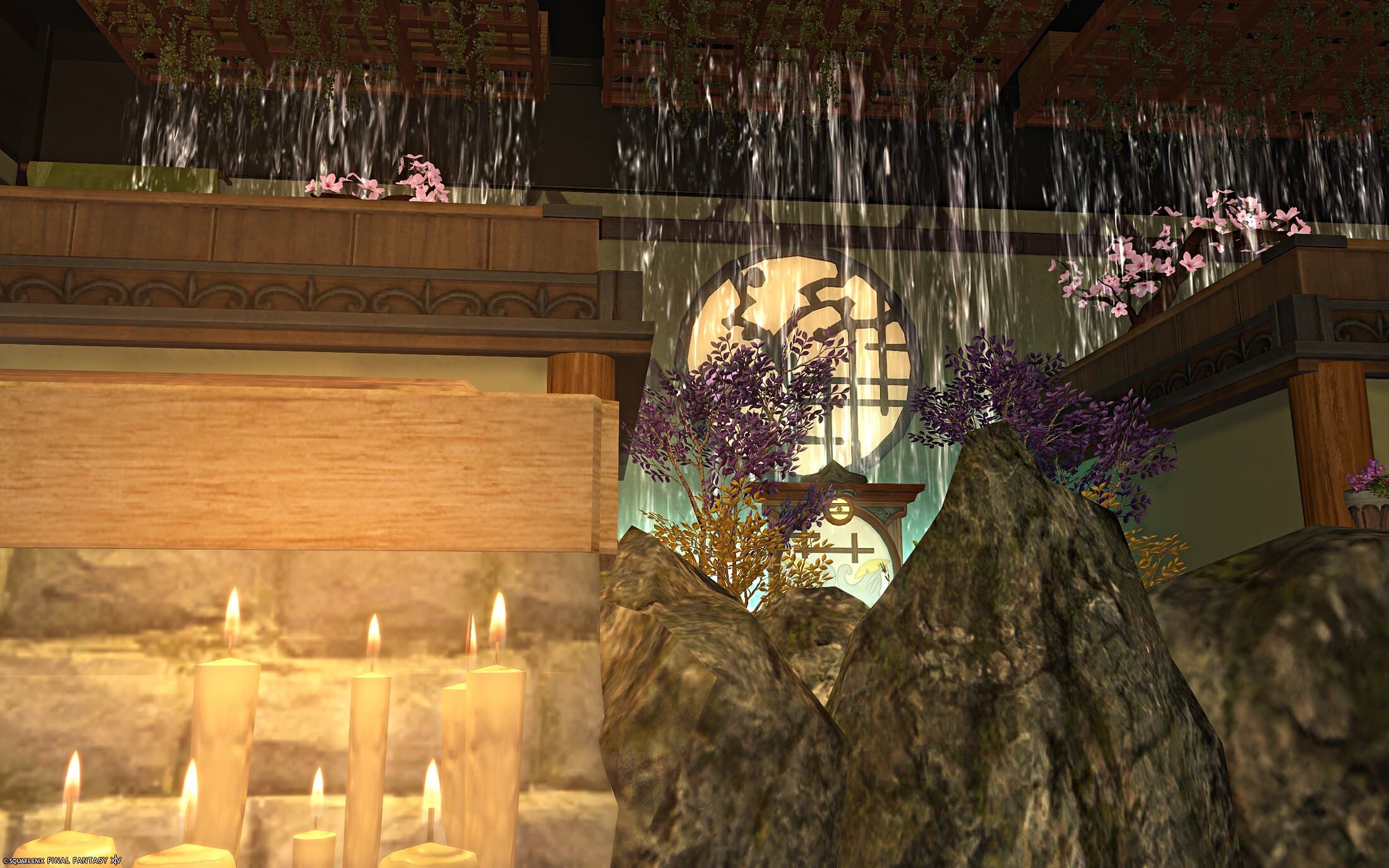 Lit candles in close-up beside the stone base of a bath, the pond rocks and the otter screen glowing behind them