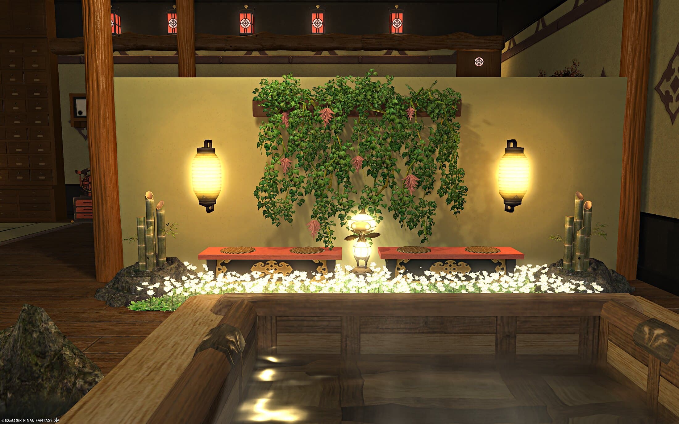 A red bench in a bed of white flowers, hanging vines on the wall above it, a paper lantern either side and bamboo at each end