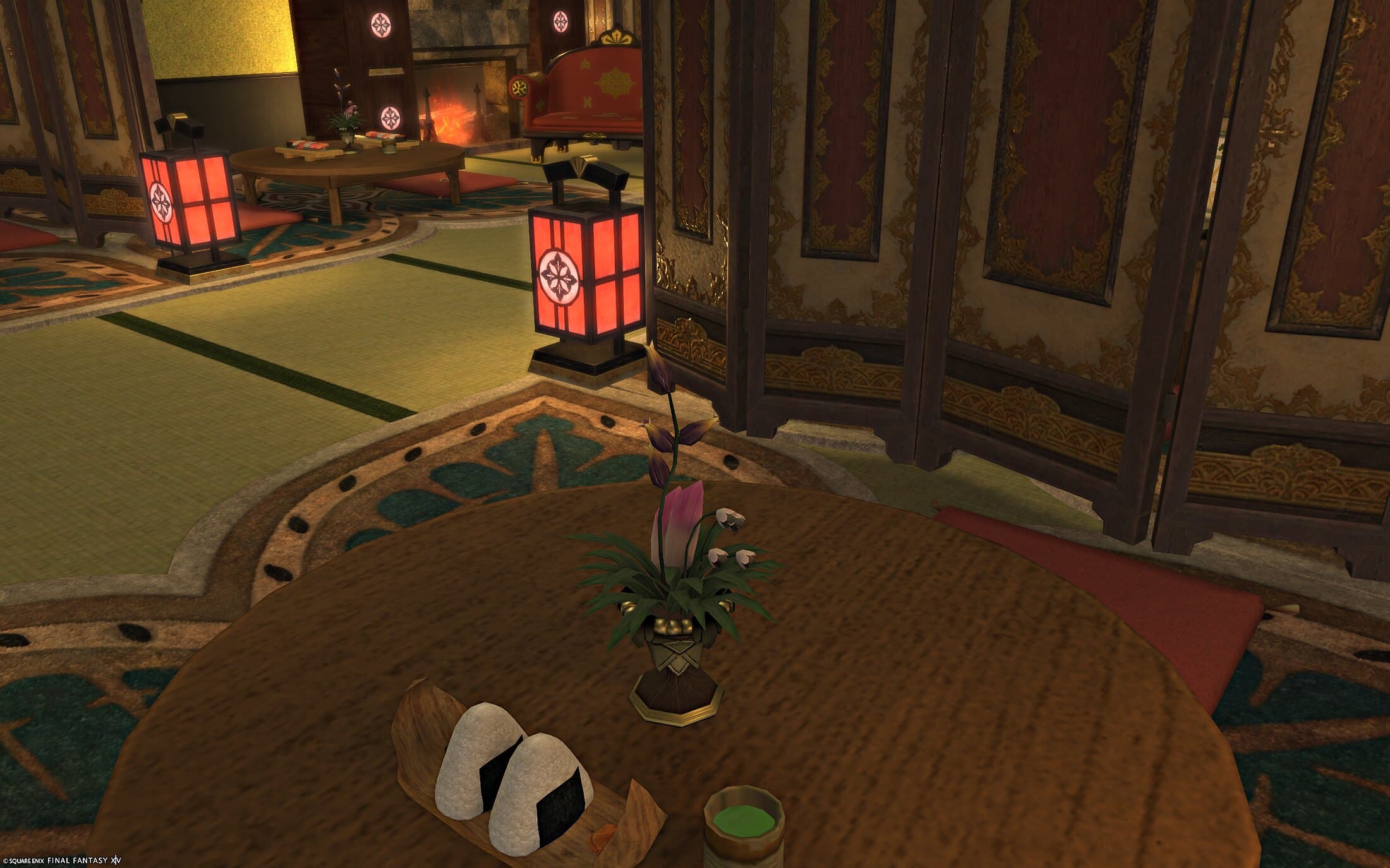 Rice balls and a cup of tea on a round table beside a flower arrangement, red lanterns and folding screens beyond