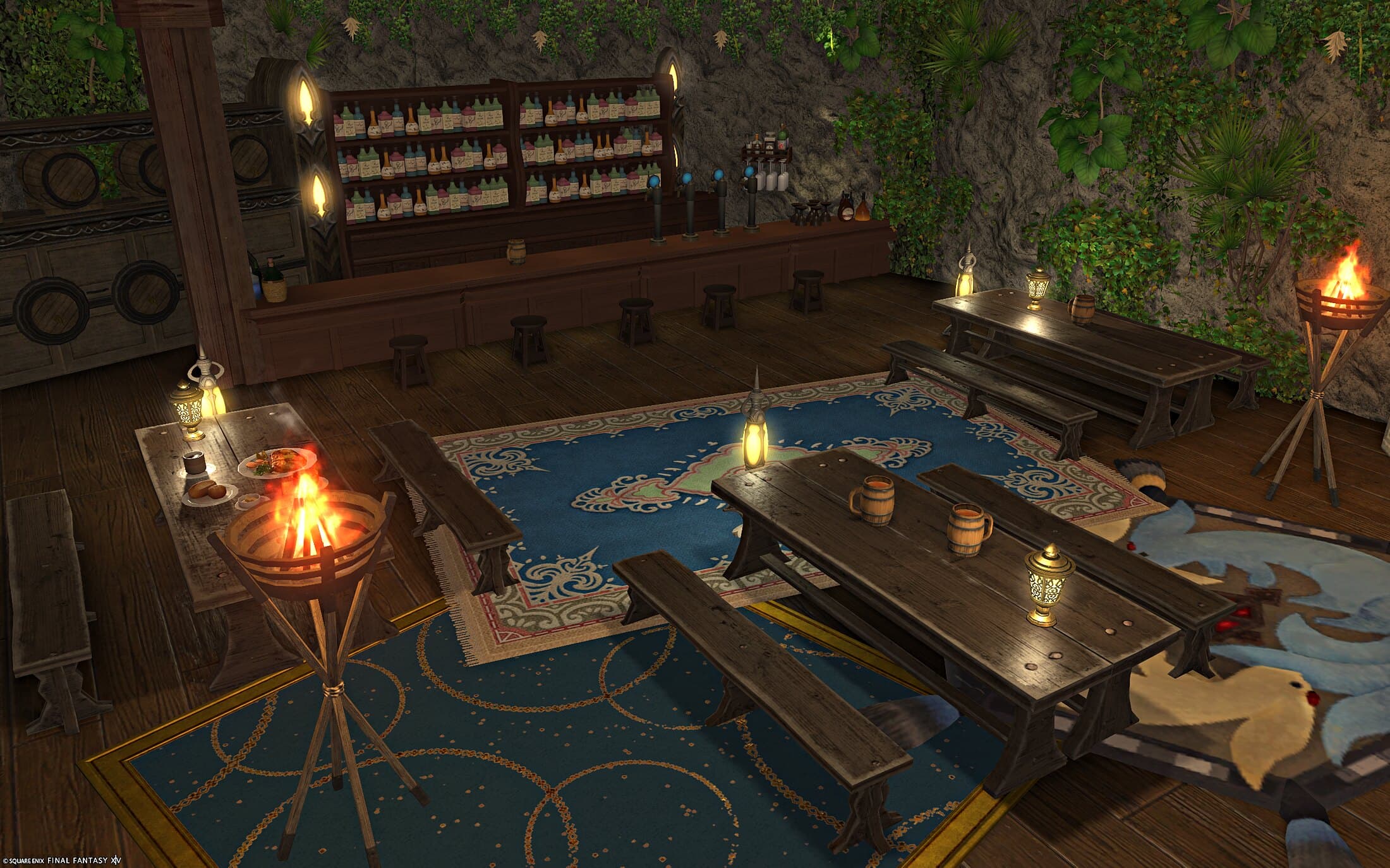 The tavern from above — long wooden tables and benches with tankards and lanterns on blue rugs, a standing fire basket burning at either side, a rug of a carbuncle at the right, and the bar behind with shelves of bottles, taps and wooden stools, a wall of barrels at the left and ivy over the rough stone