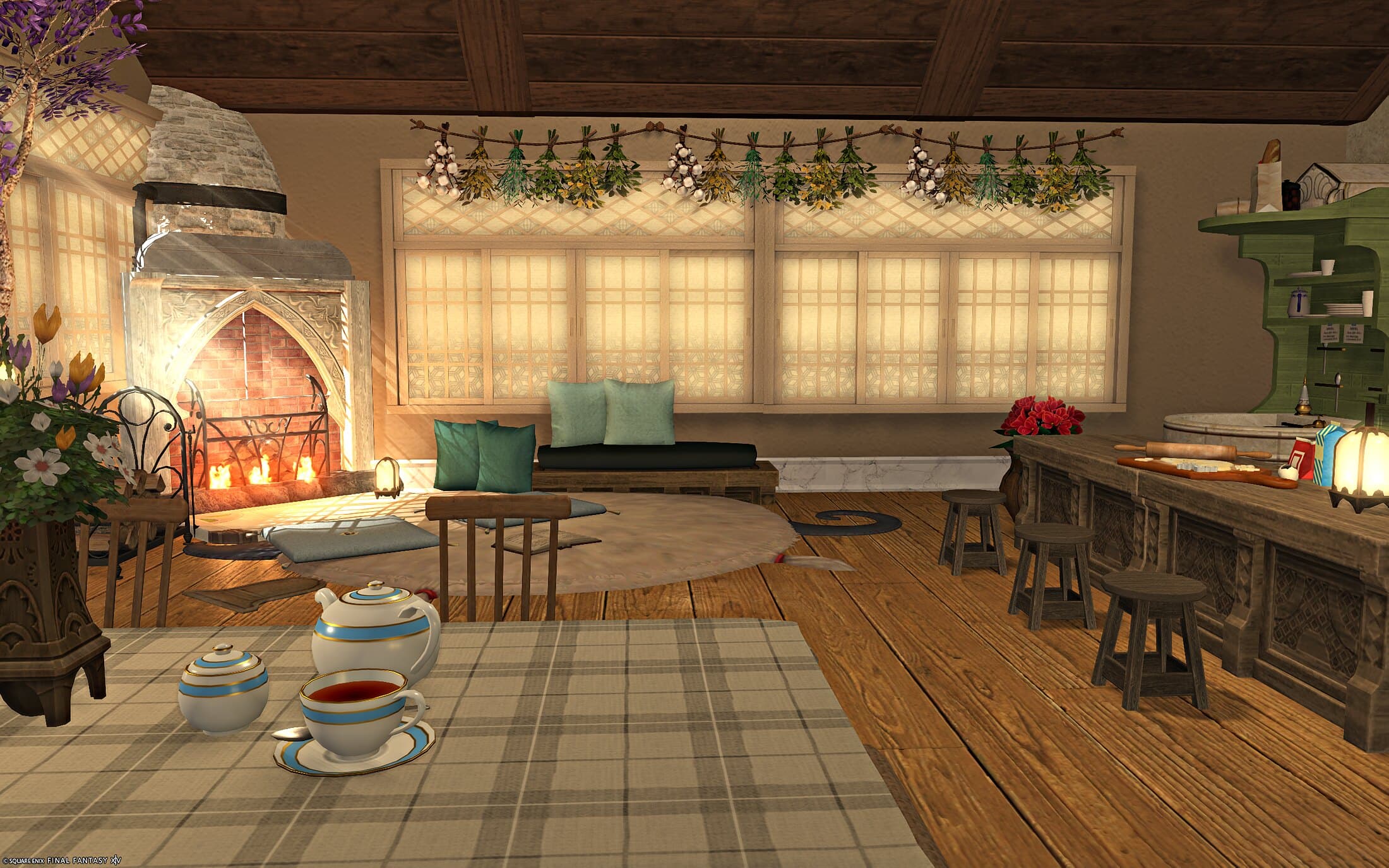 The dining table laid with a blue-and-white tea set on a plaid cloth, the fireplace glowing at the left and the kitchen counter beginning at the right