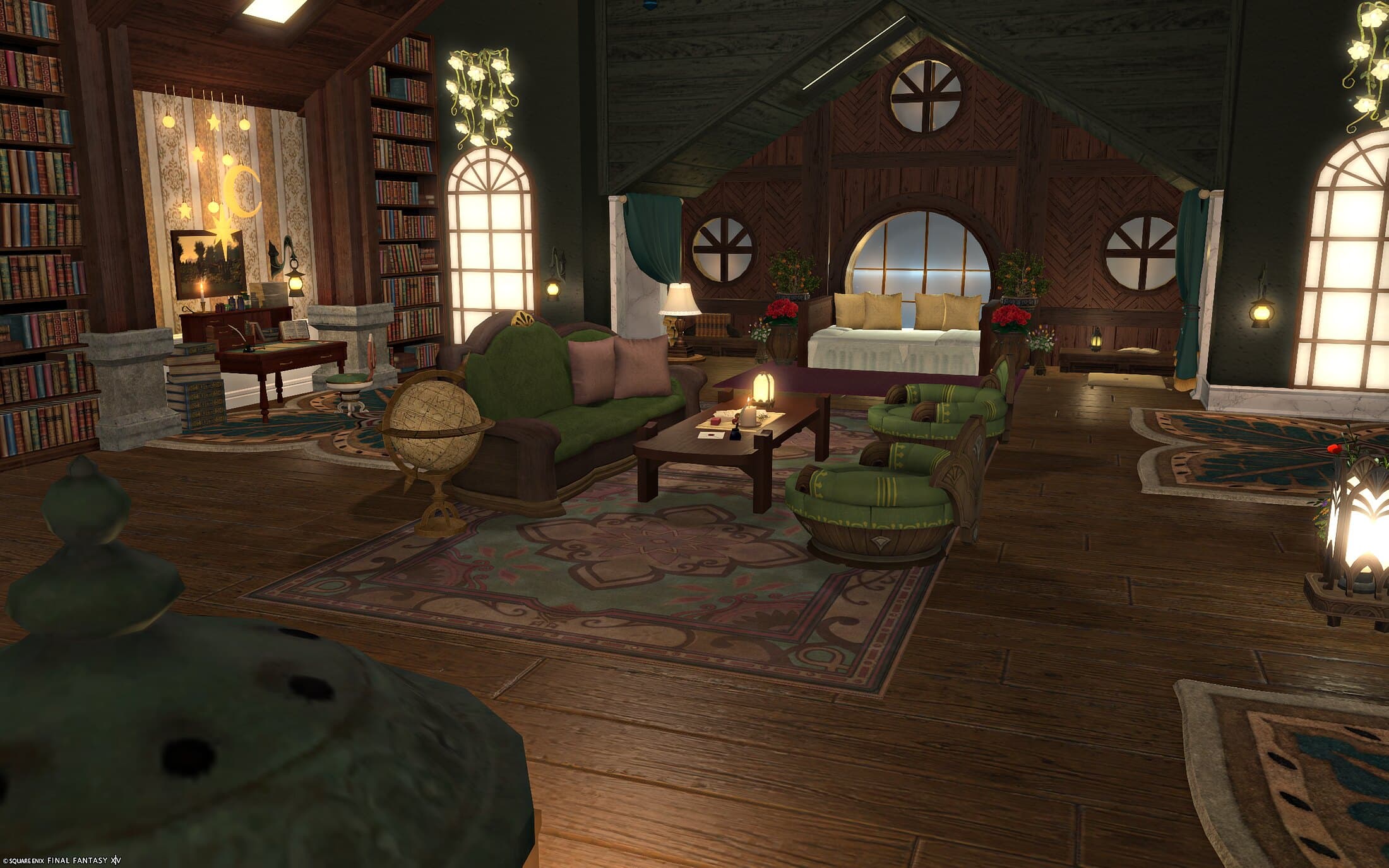 The desk alcove and sofa seen together, a round window above the bed glowing at the back of the room, another round window mirrored above the desk