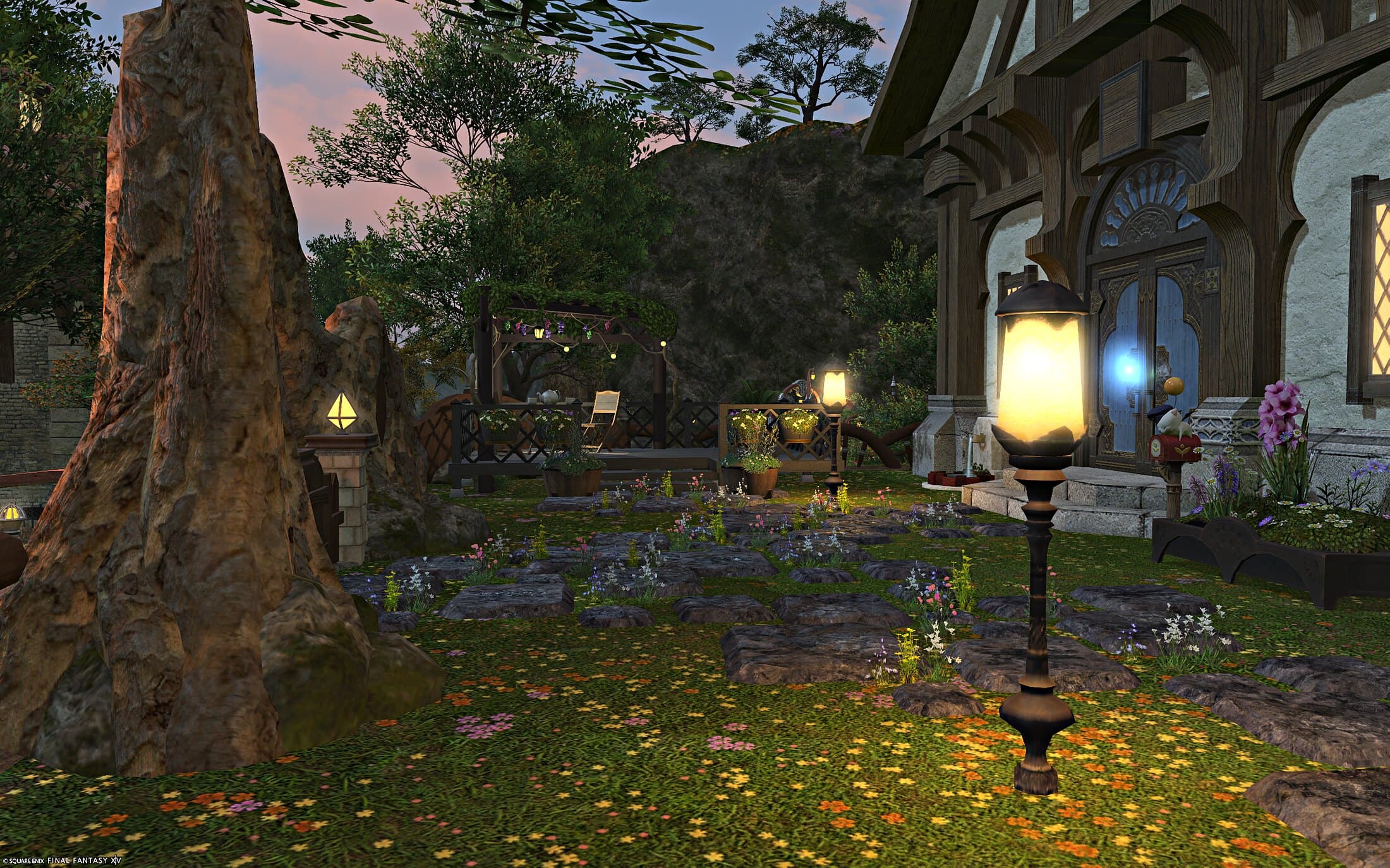 The cottage's exterior at dusk, timber and white stone under Twelveswood trees, a lit lamp post on the flower-strewn lawn