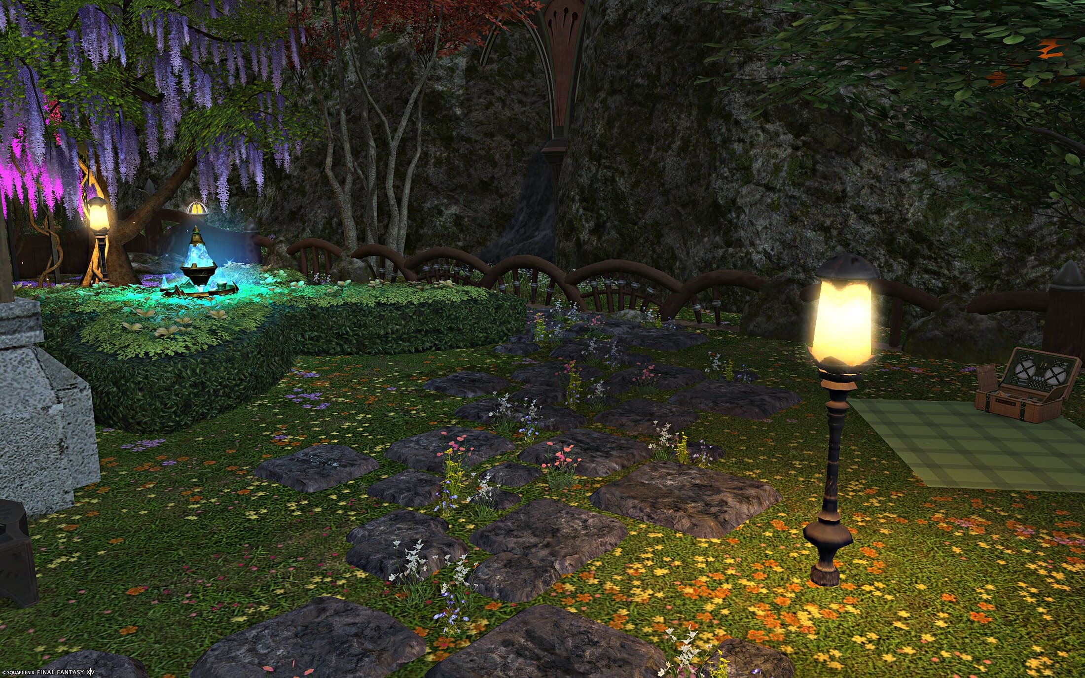 A garden hedge shaped in a cross, a glowing blue-green fountain ornament at its centre, wisteria hanging from the trees above and a lamp post beside it