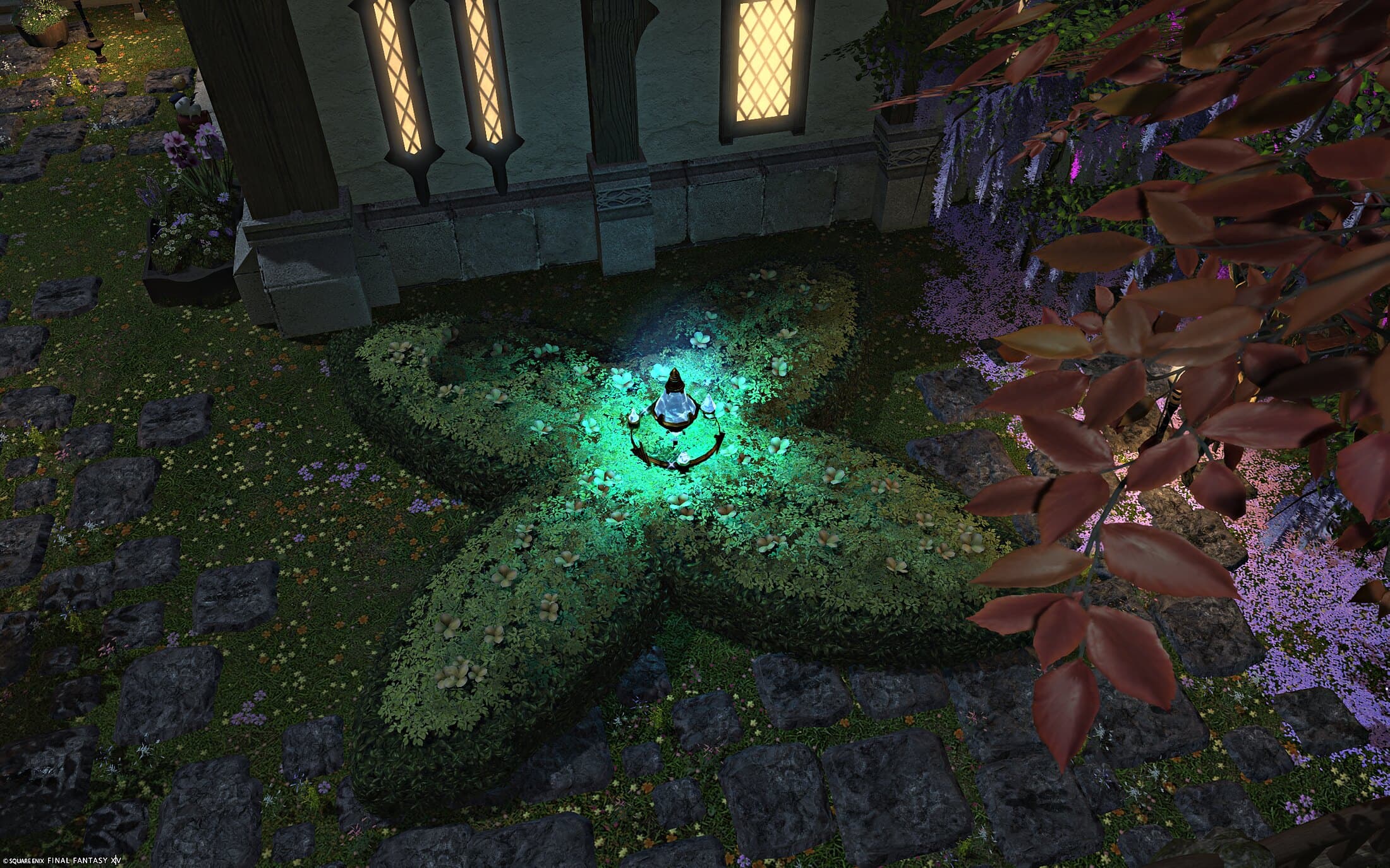 The star-shaped hedge close up, its fountain ornament glowing green, autumn leaves drifting over the stone path beside the house